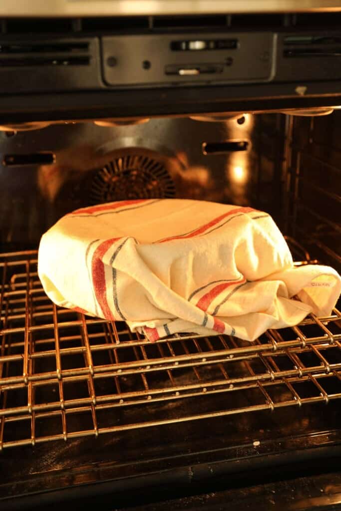 Dough covered with a kitchen towel rising in the oven