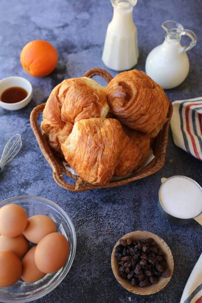 Croissants in a basket and other ingredients for bread pudding laid out on a counter