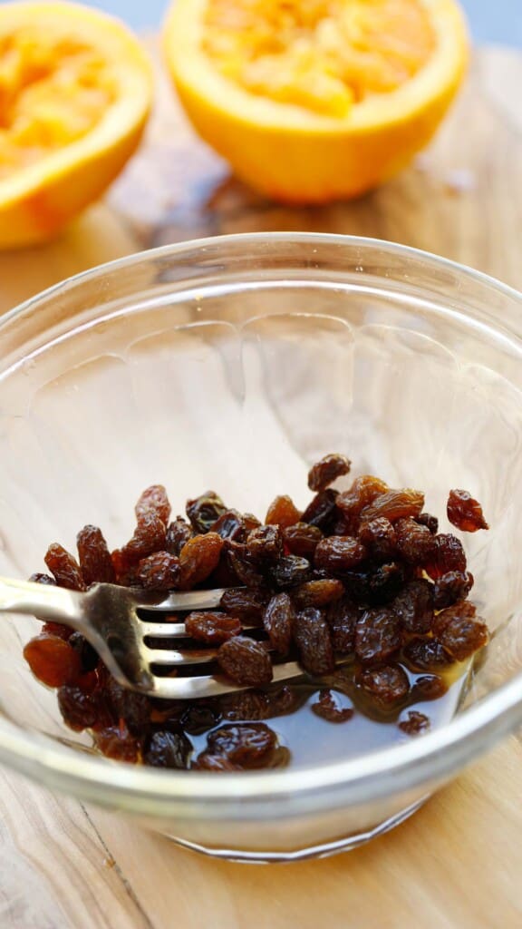 A clear bowl with raisins soaking in orange juice