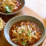 Two bowls of soup topped with chicken, cheese and tortillas