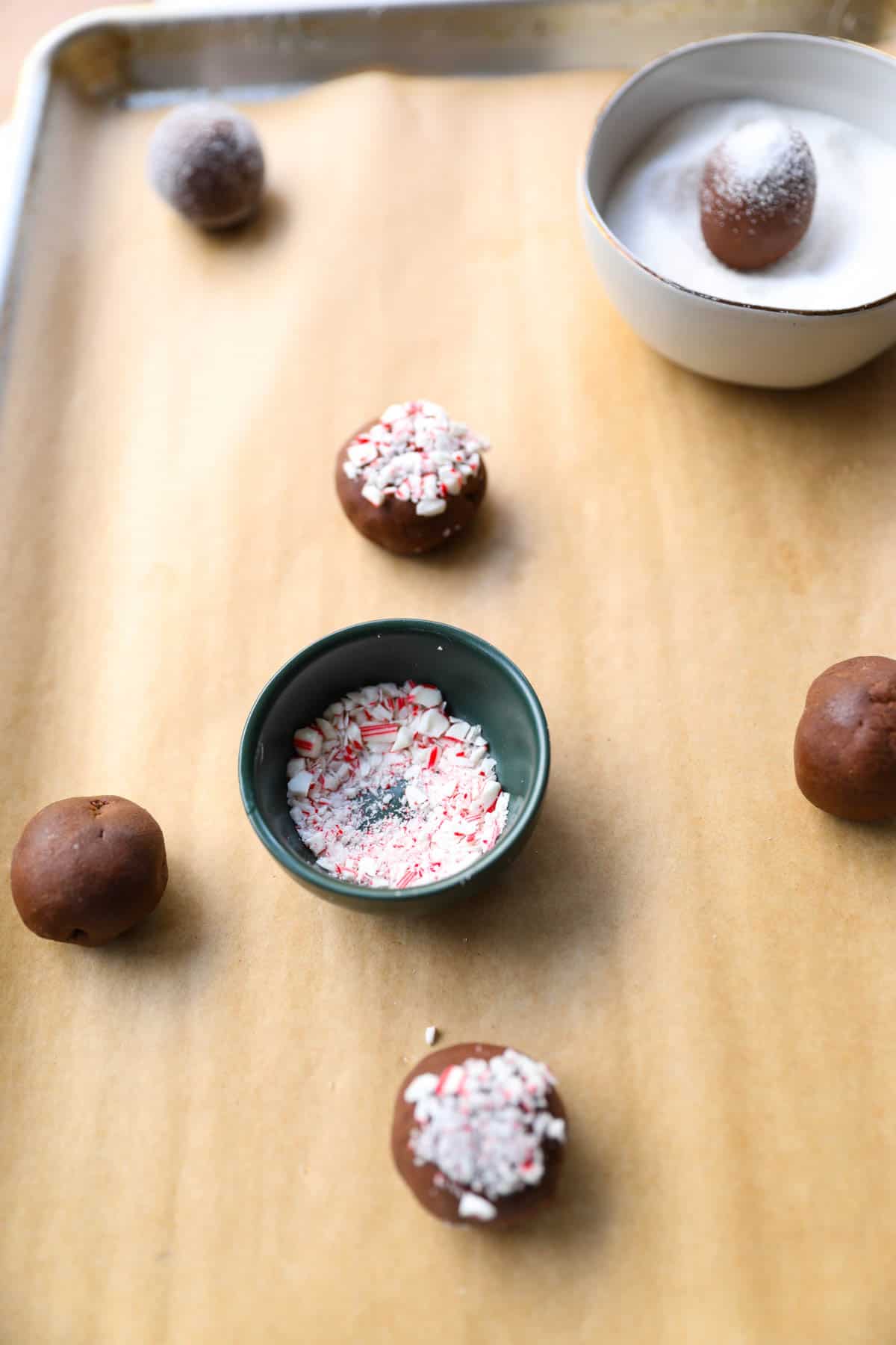 Dough balls being riolled in sugar and candy canes that have been crushed