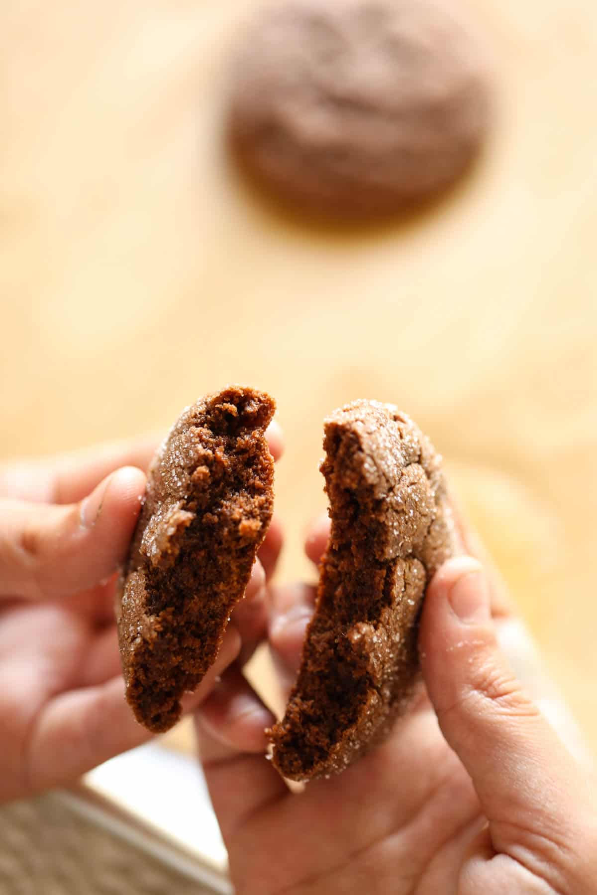 A child's hand breaking apart a soft chocolate cookie to show the interior