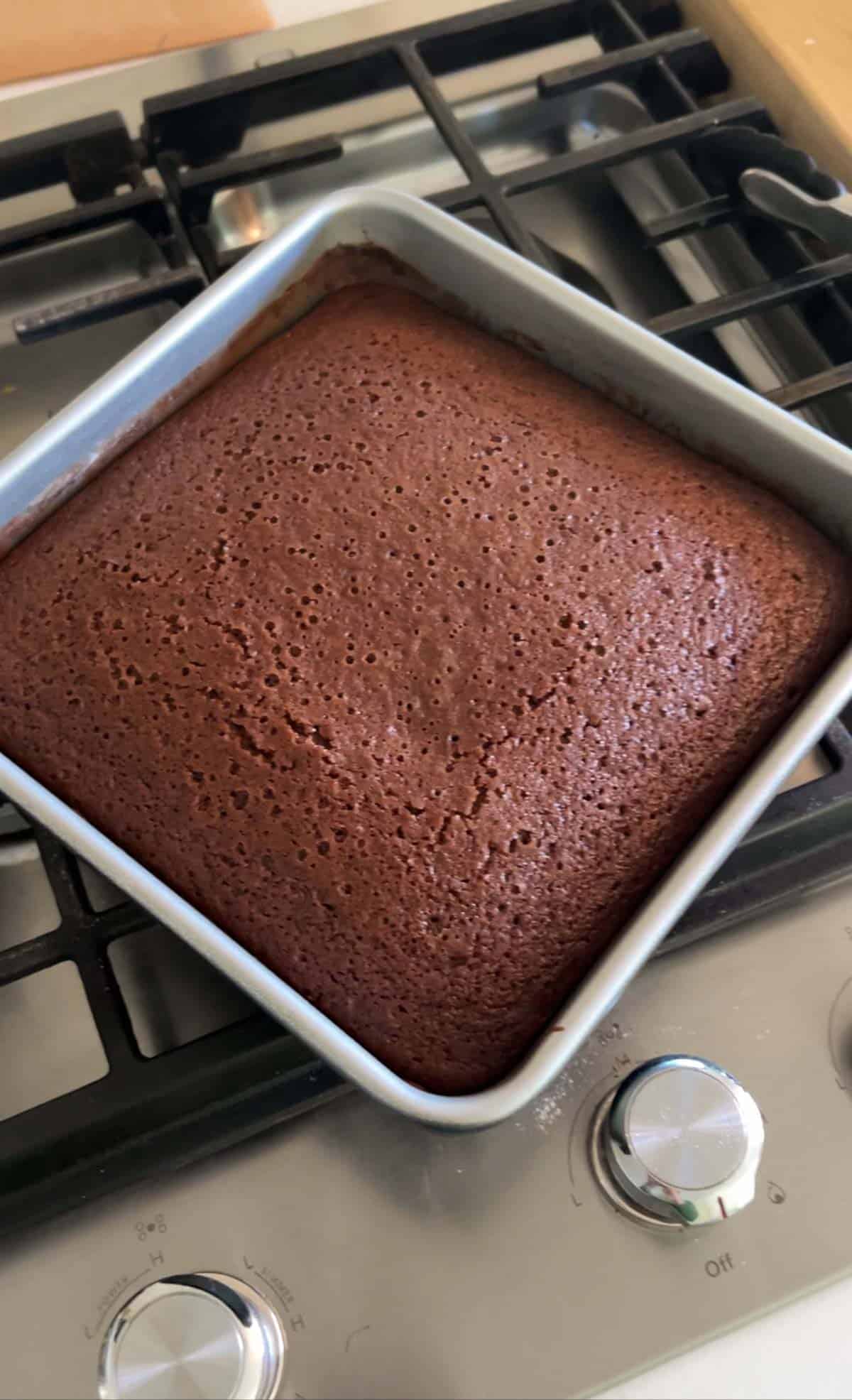 A chocolate cake in a square pan freshly baked cooling on cooktop
