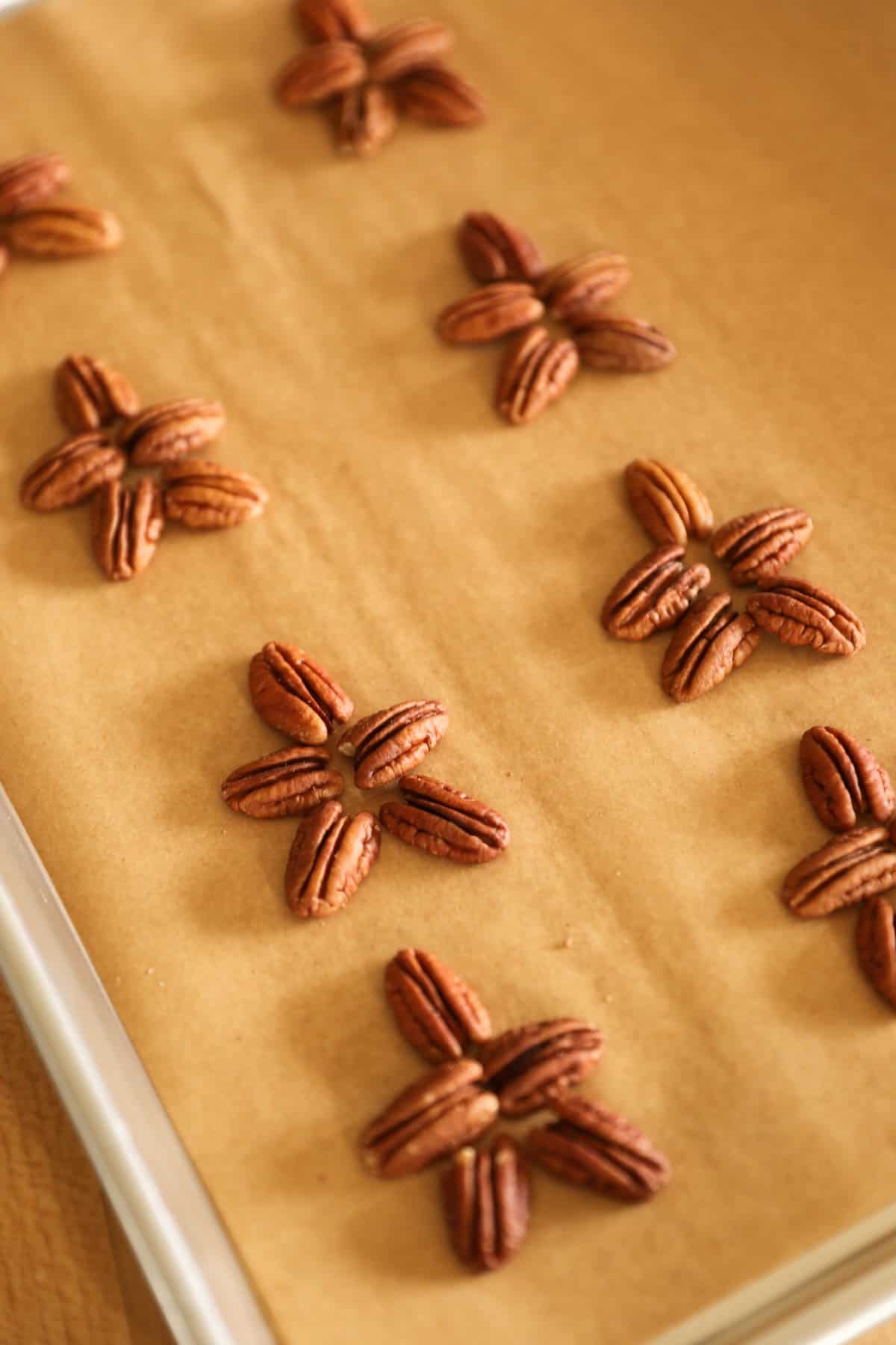 Pecans laid out in the form of turtles on a parchment lined cookie sheet