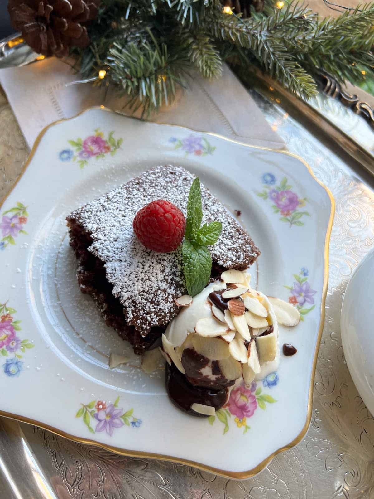 a finished slice of chocolate wacky cake on a china plate with ice cream and hot fudge