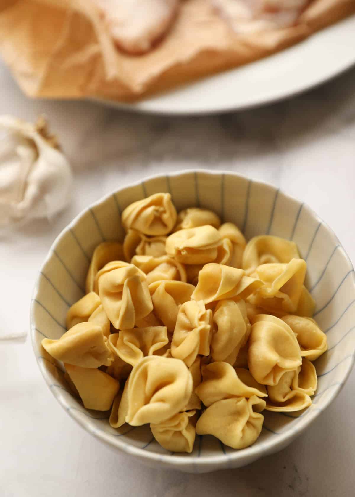 small cheese tortellini in a bowl with chicken in the background