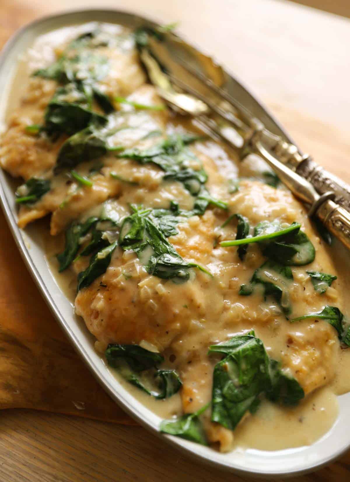 A platter of seared chicken in a creamy sauce with wilted spinach