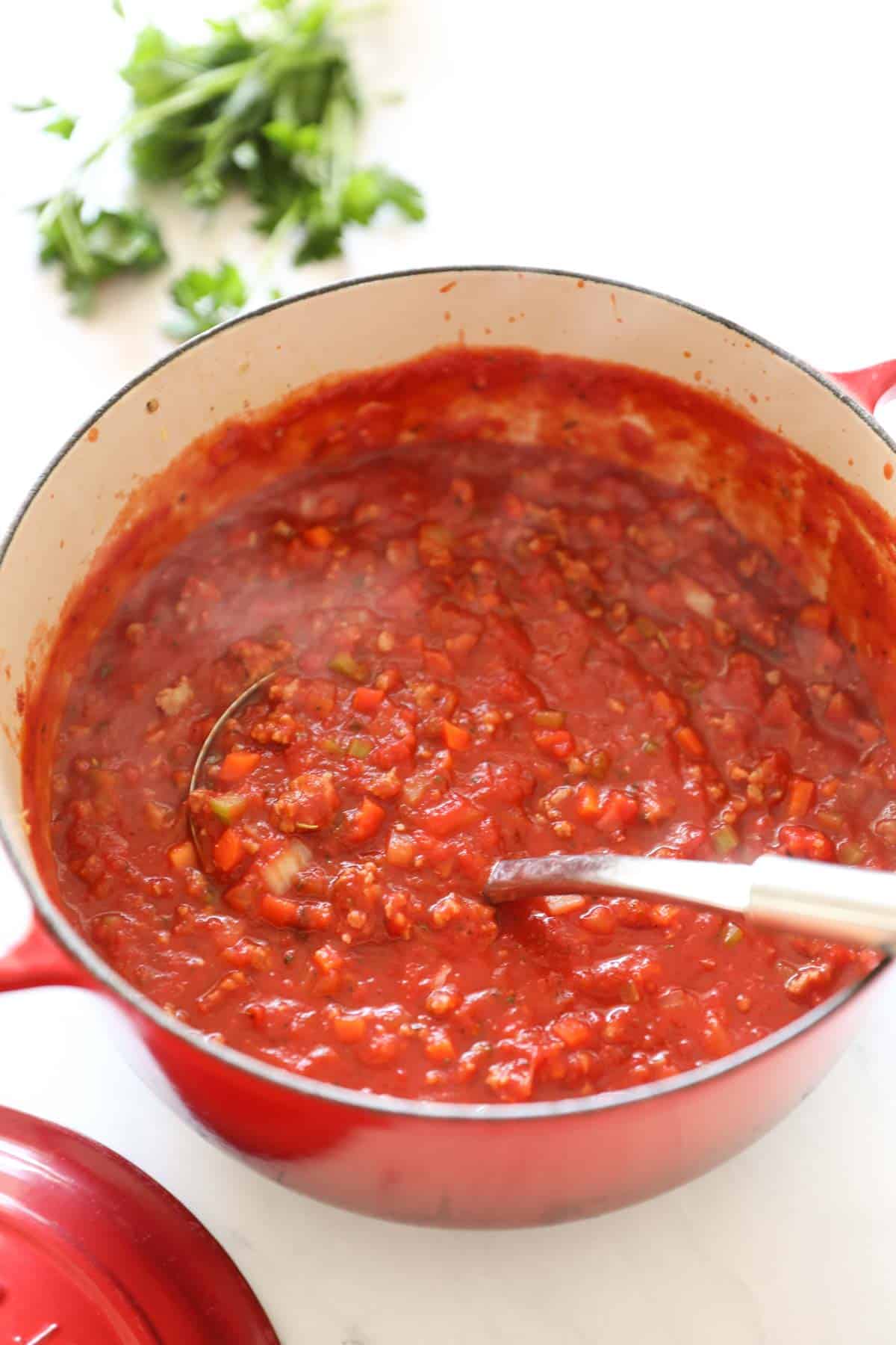 a red Dutch oven filled with simmering tomato sauce