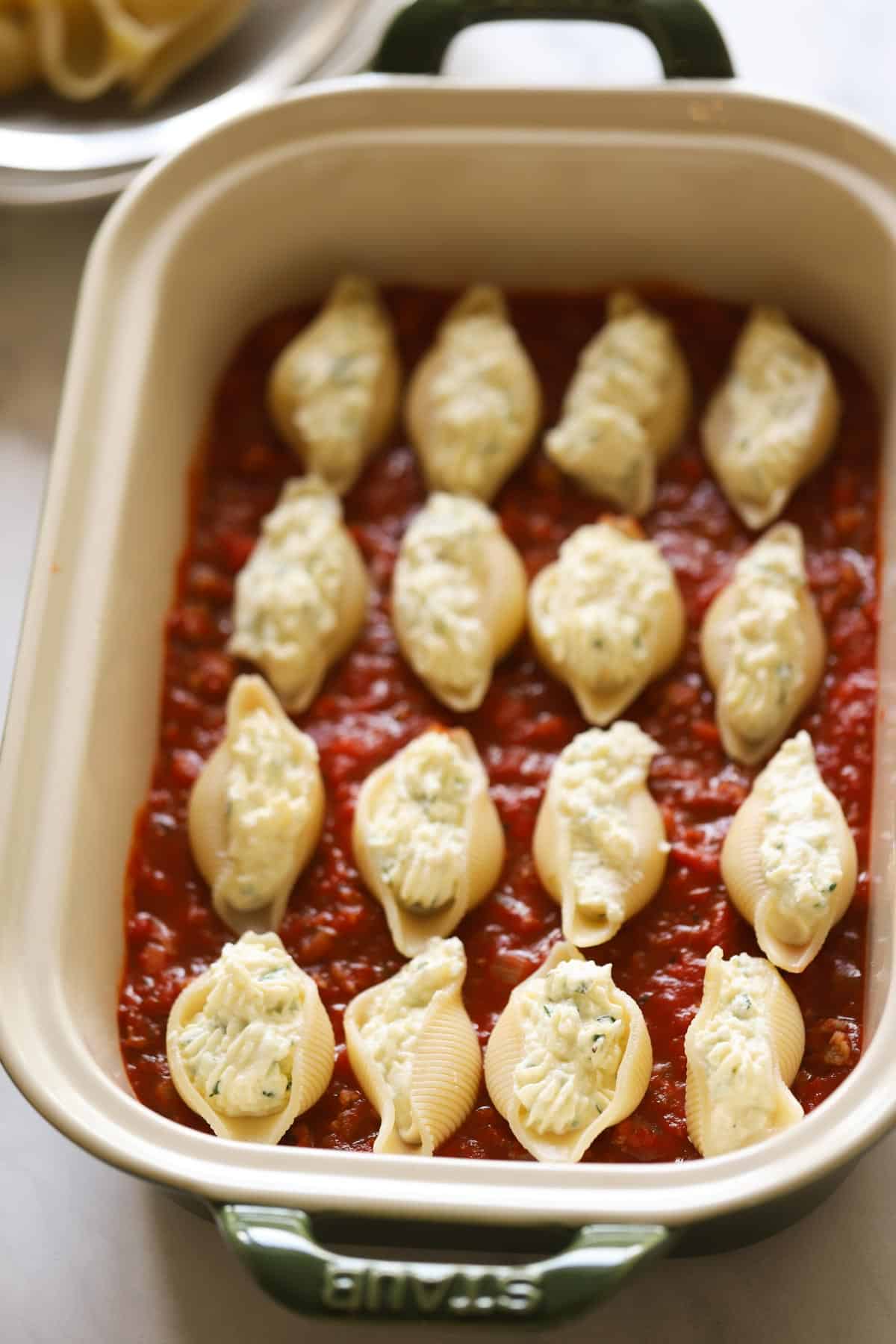 a green casserole with a bed of tomato sauce topped stuffed shells