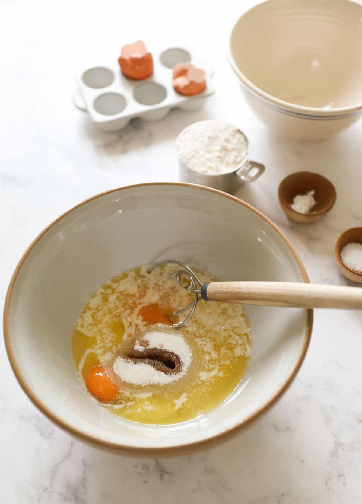 a bowl of wet ingredients with a danish dough whisk and dry ingredients in the background