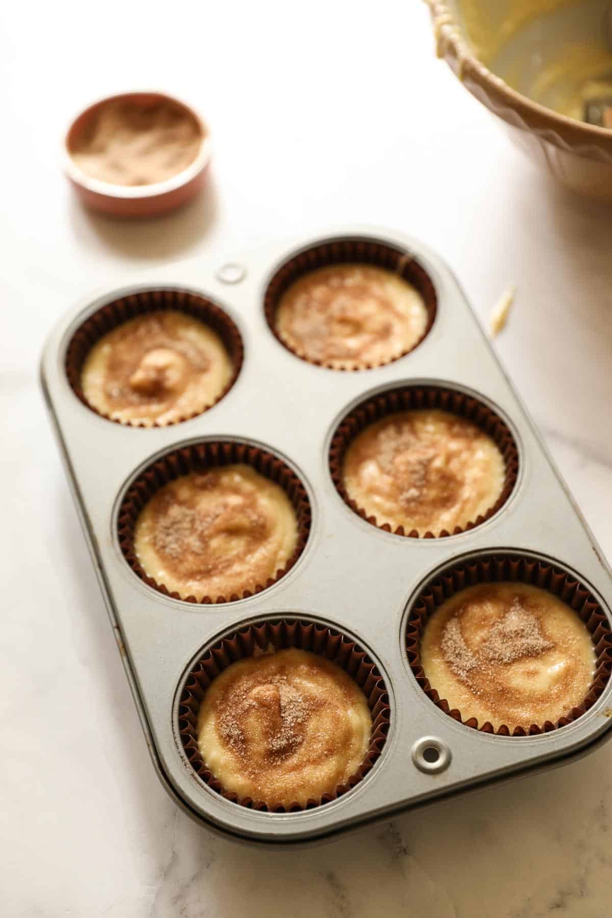 muffin batter in a 6-well jumbo muffin tin sprinkled with cinnamon sugar