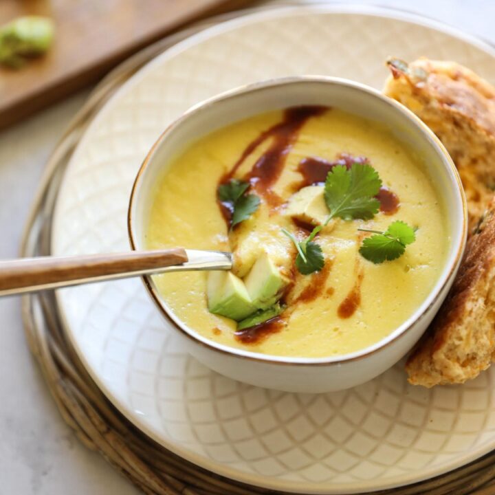 Corn soup in a bowl with avocado and cilantro and hot sauce
