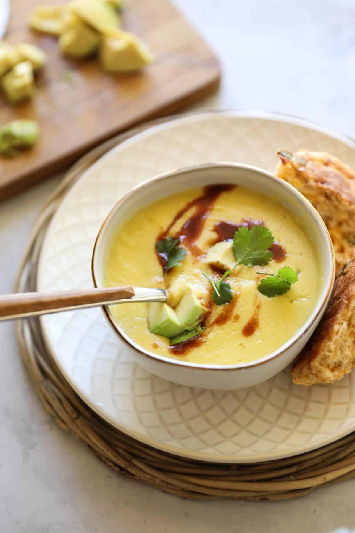creamy corn soup with hot sauce swirled into it topped with avocado and cilantro