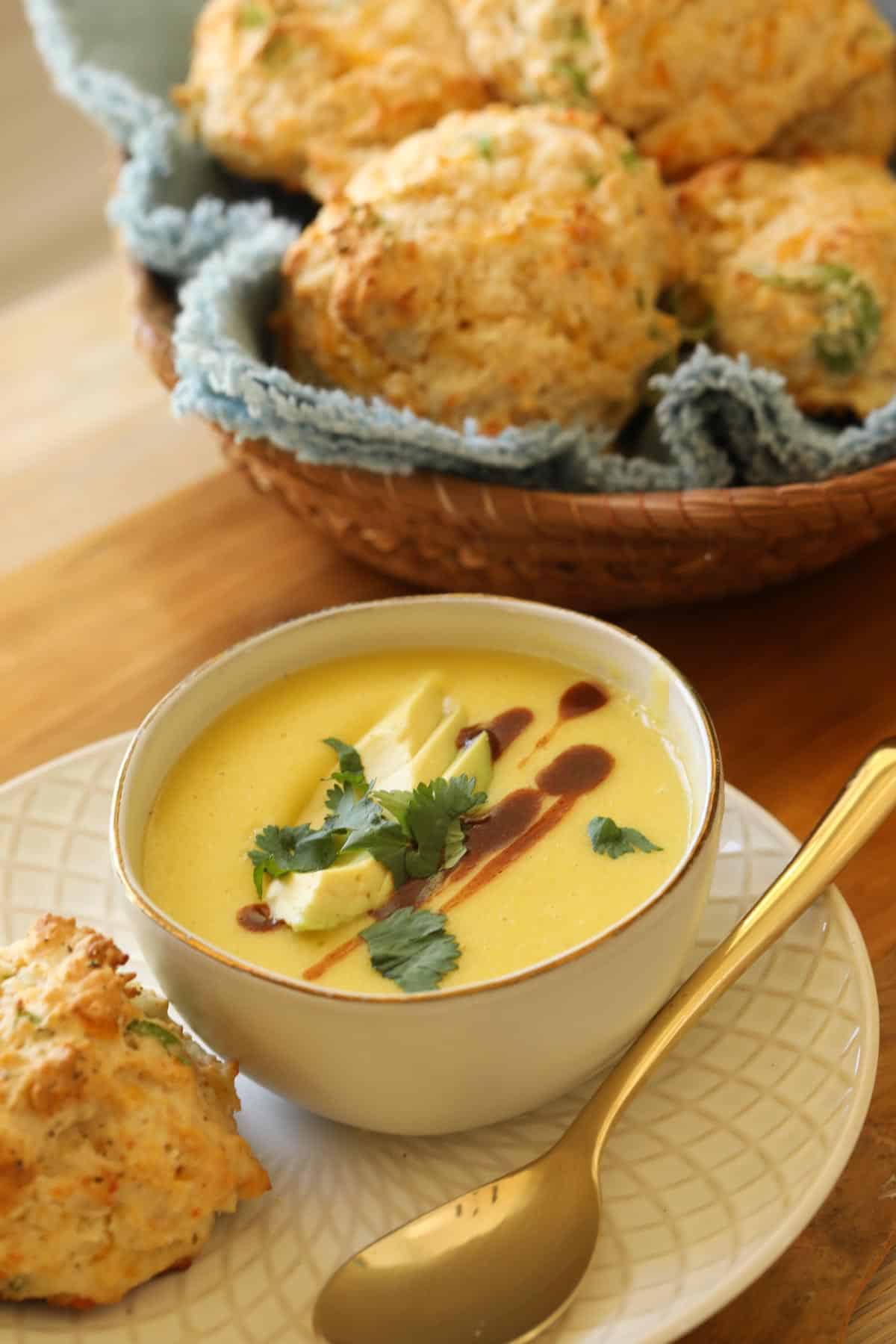 a bowl of corn soup topped with hot sauce avocado and cilantro with cheesy biscuits