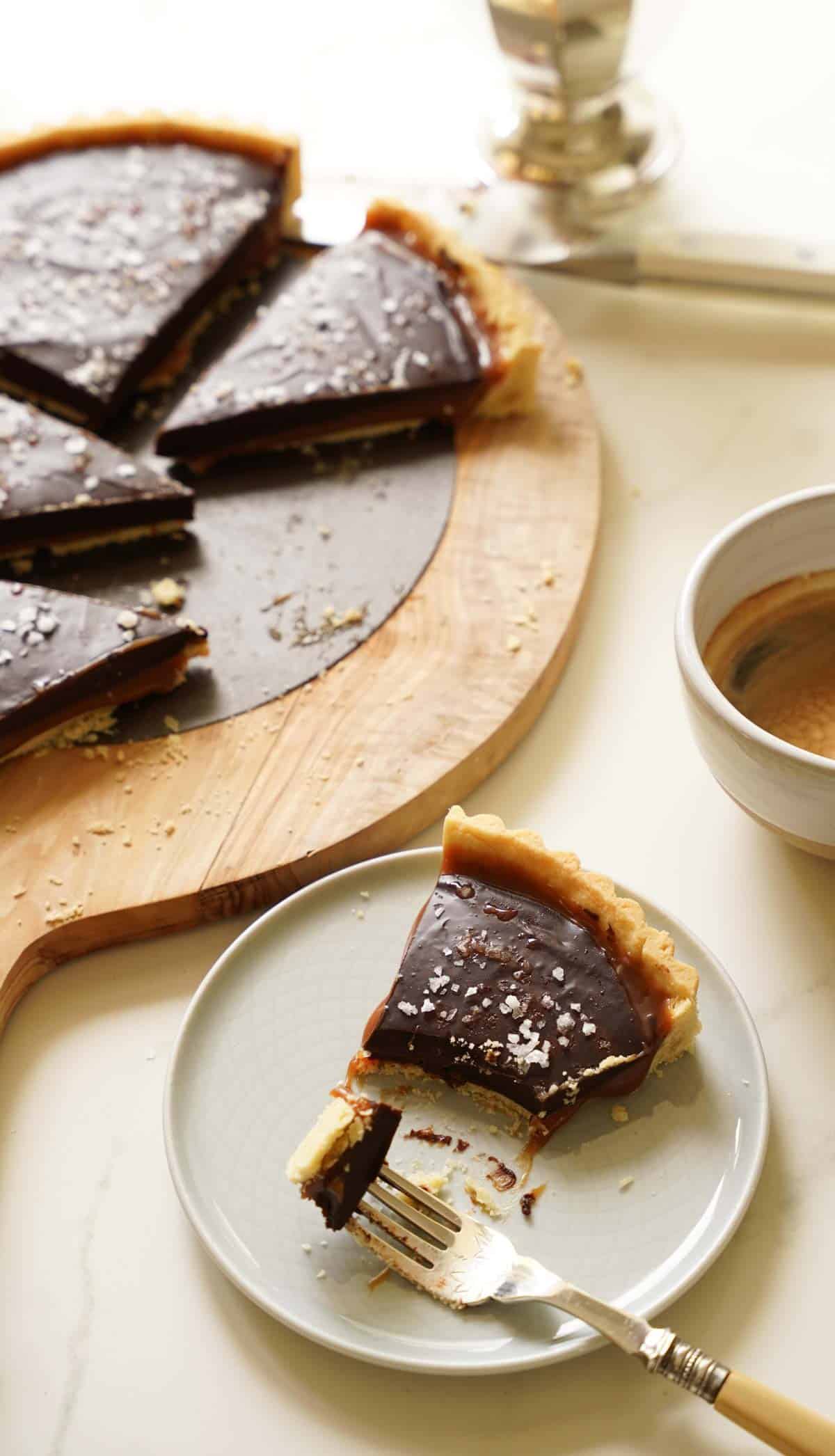 a slice of chocolate caramel tart on a plate with a bite taken out