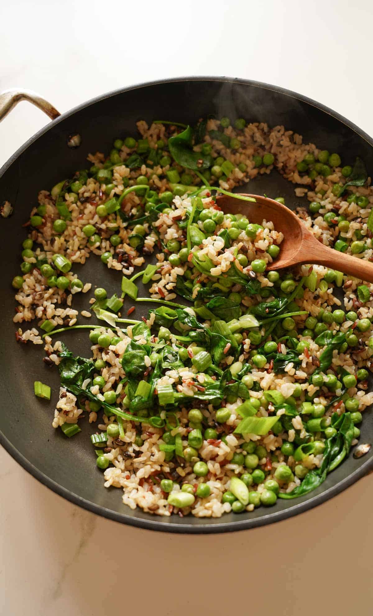 stir-fried rice blend in a pan with veggies and a wooden spoon.