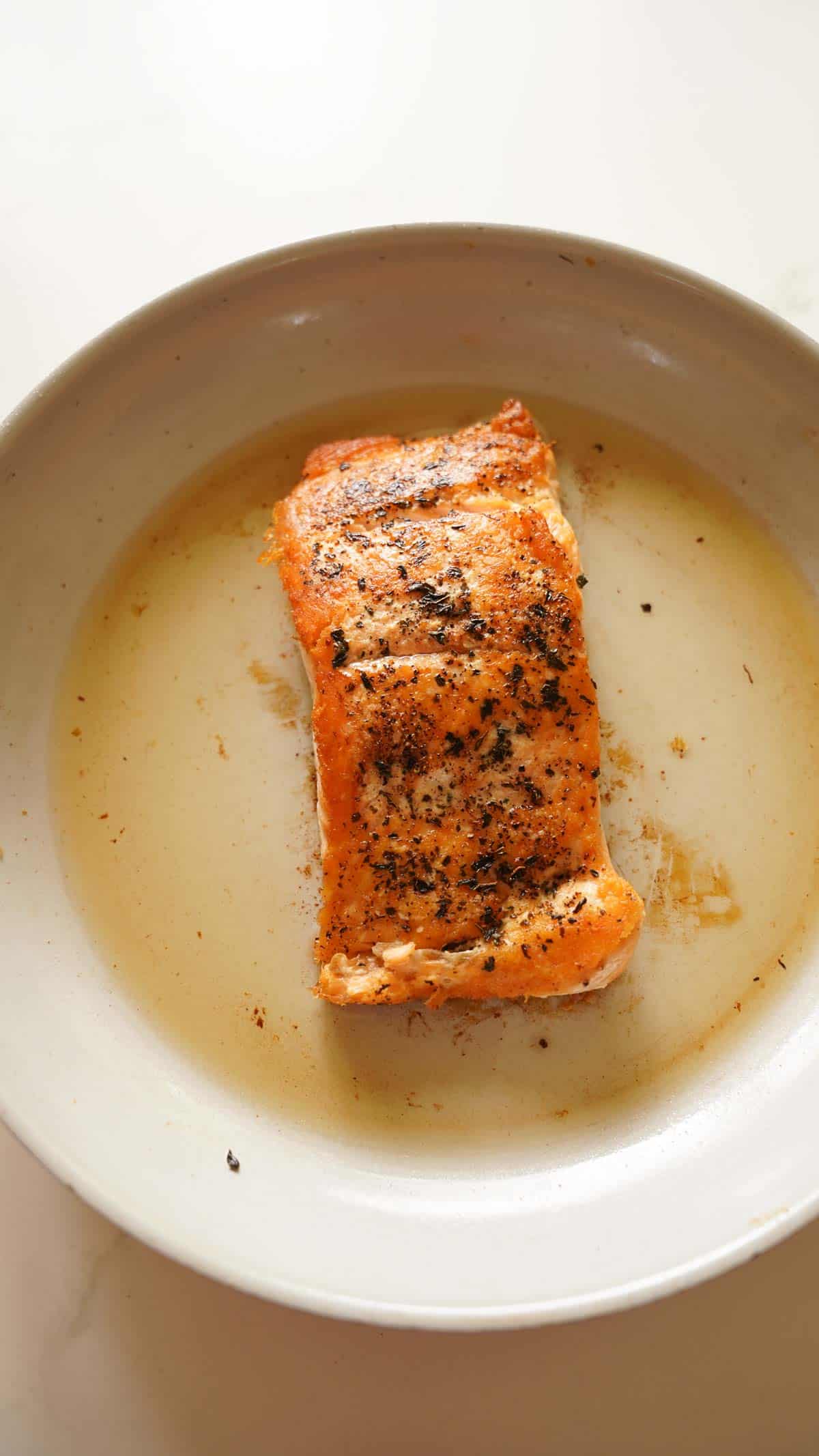 filet of salmon seared in a pan with seasoning on top
