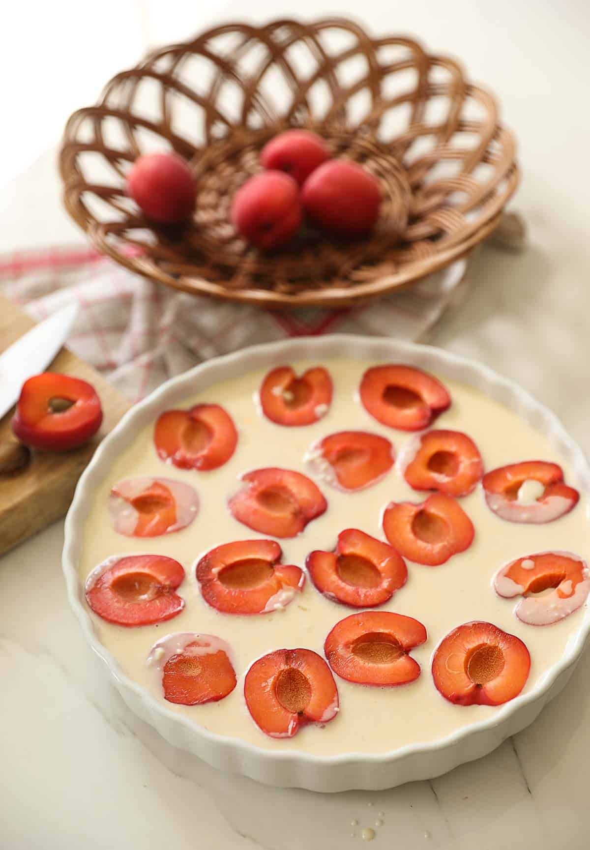 apricot halves being placed in clafoutis batter in a pie plate.