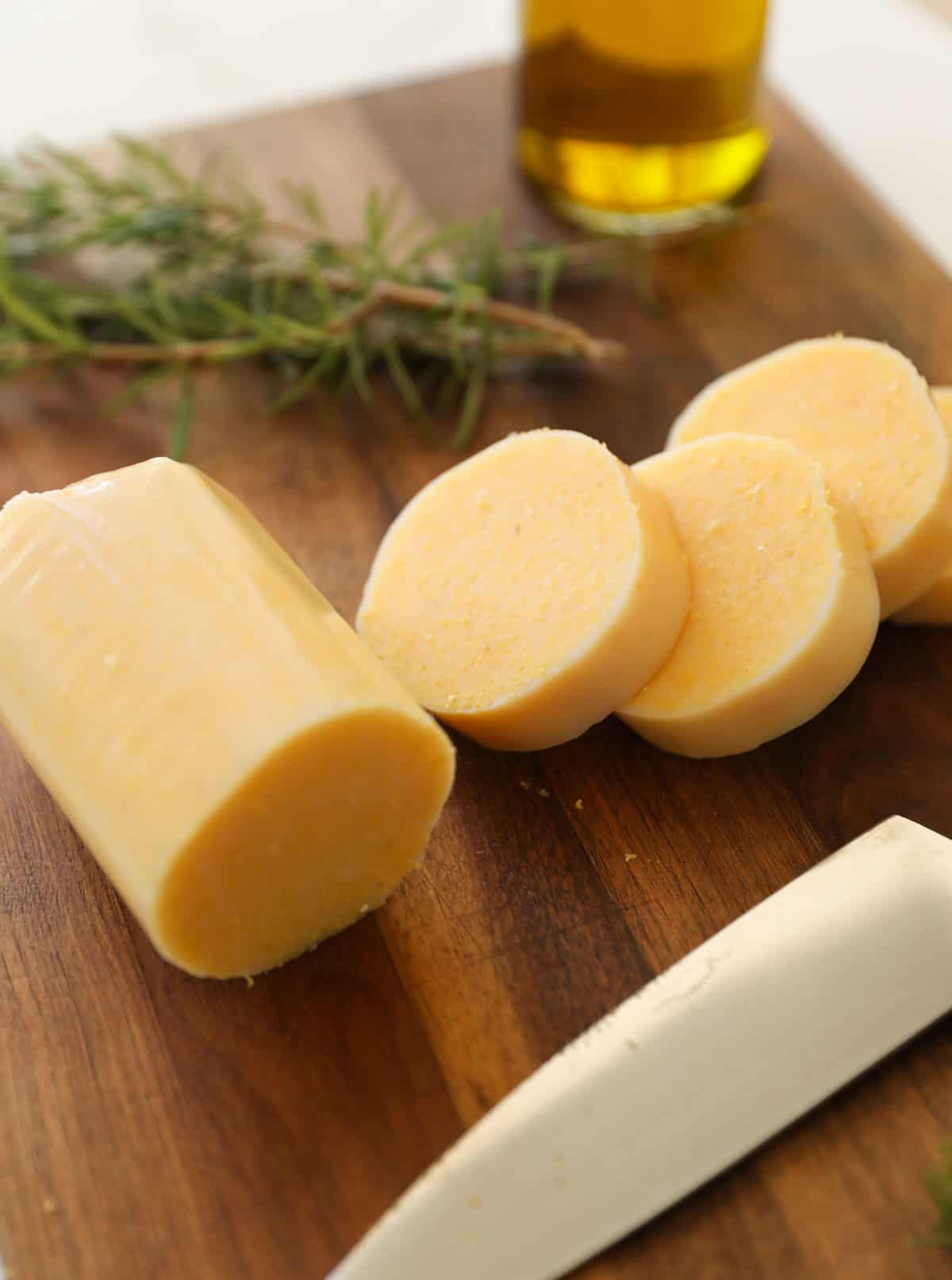 sliced tubed polenta on a cutting board with rosemary and olive oil