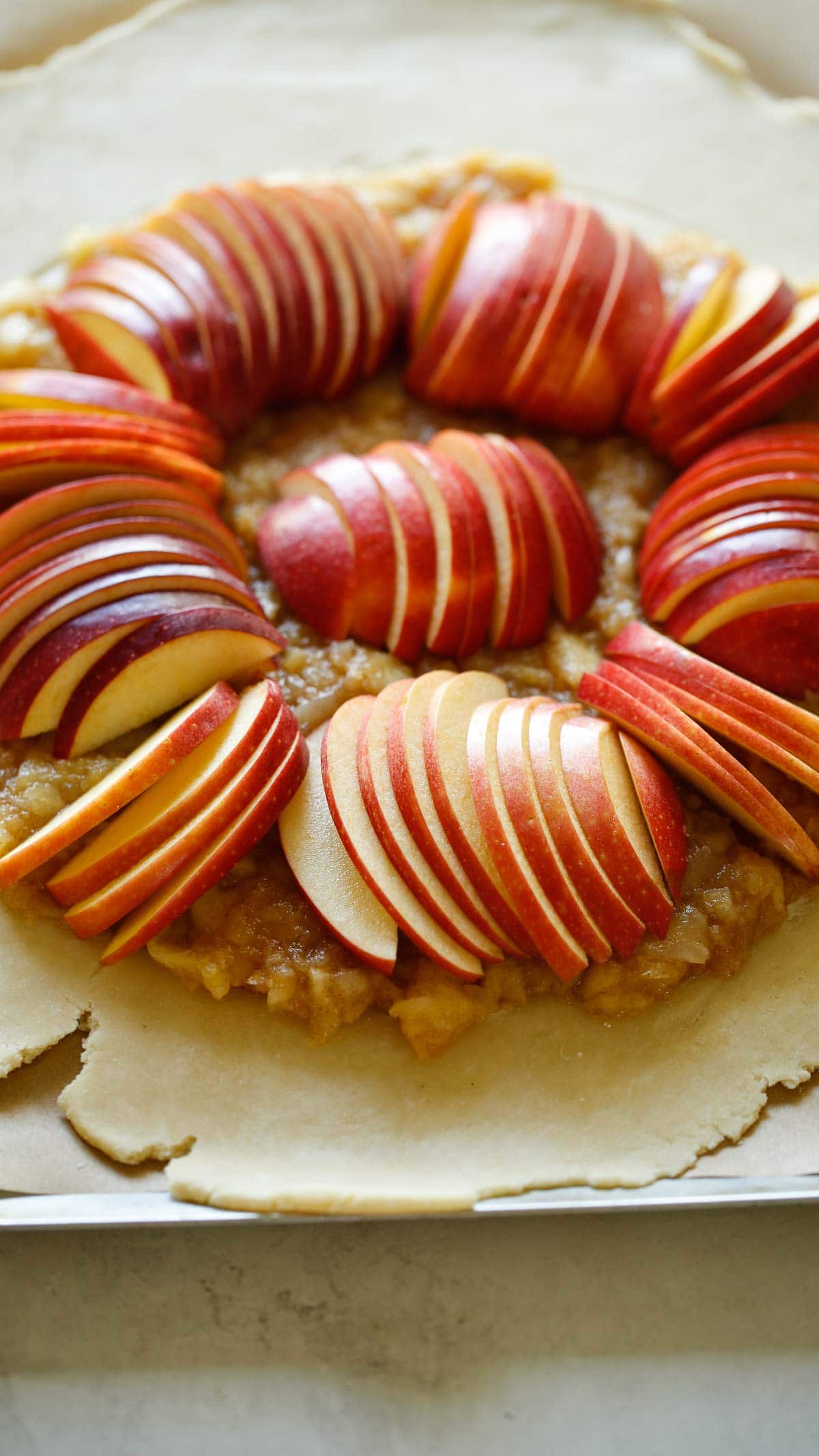 dough rolled out to a circle with apple compote in the center and apples fanned out in slices on top