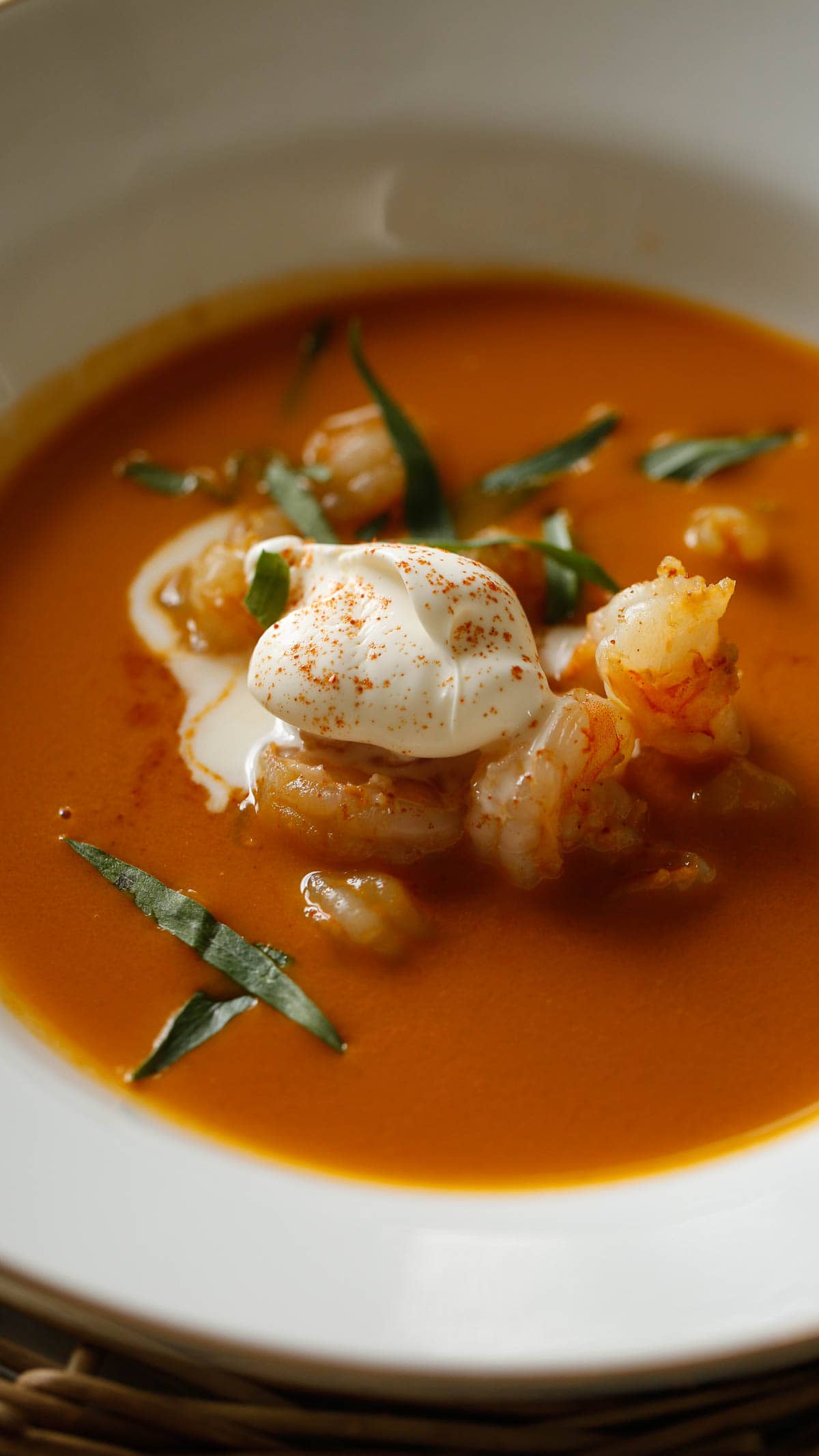 Shrimp Bisque in a white shallow bowl topped with creme fraiche and tarragon