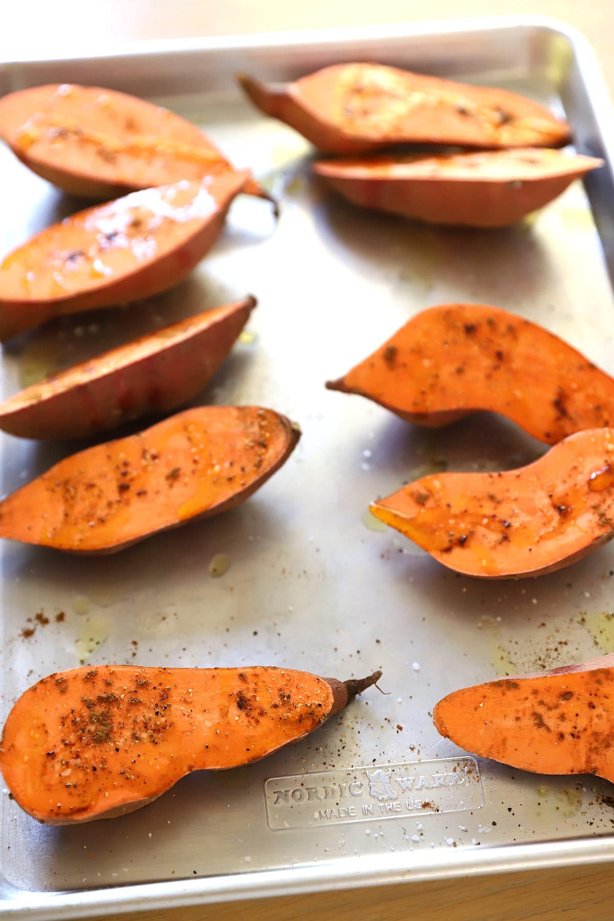 Raw sweet potatoes sliced in half on a baling sheet with seasoning