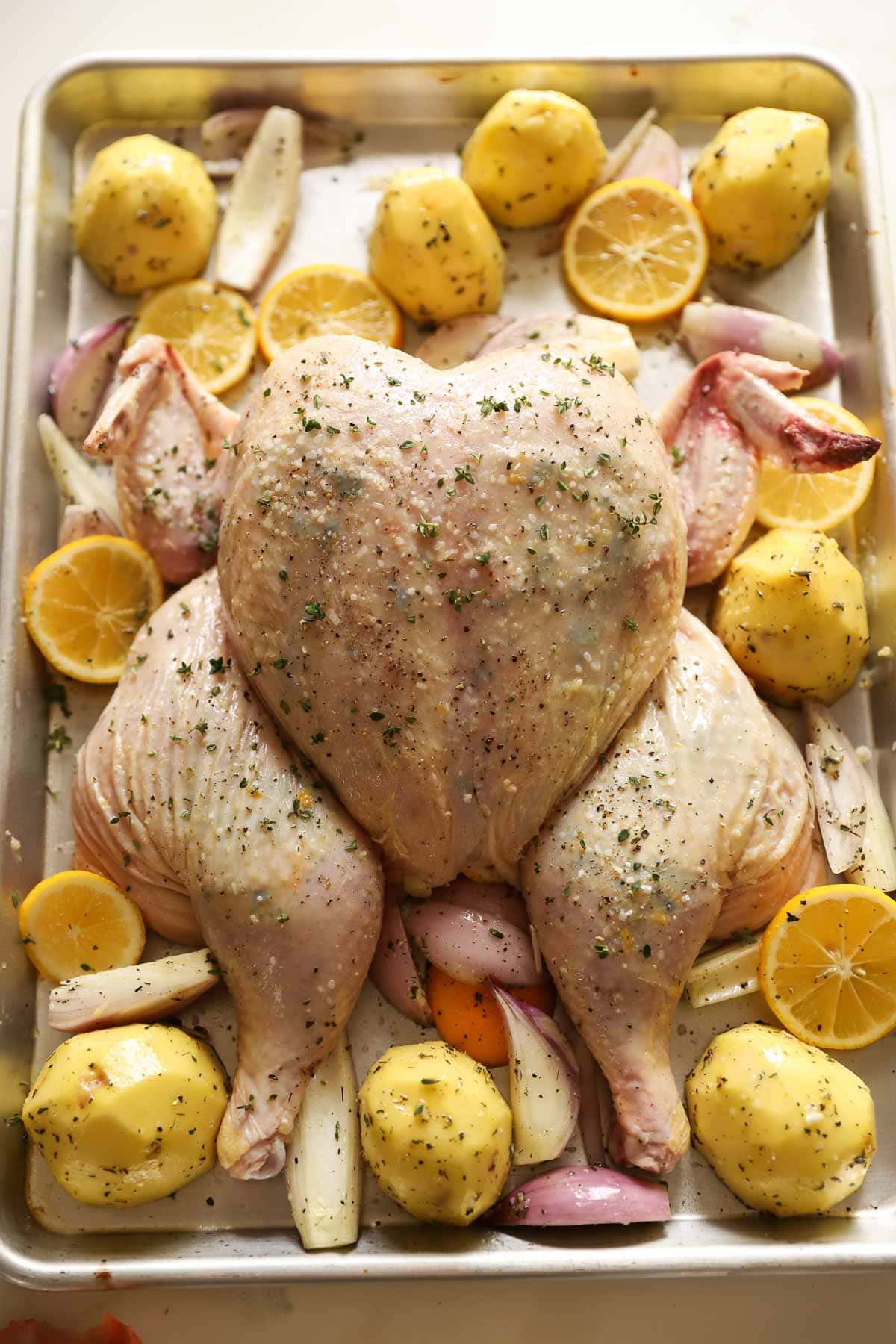 a whole chicken on a sheet pan with potatoes, lemon and shallots ready for the oven.