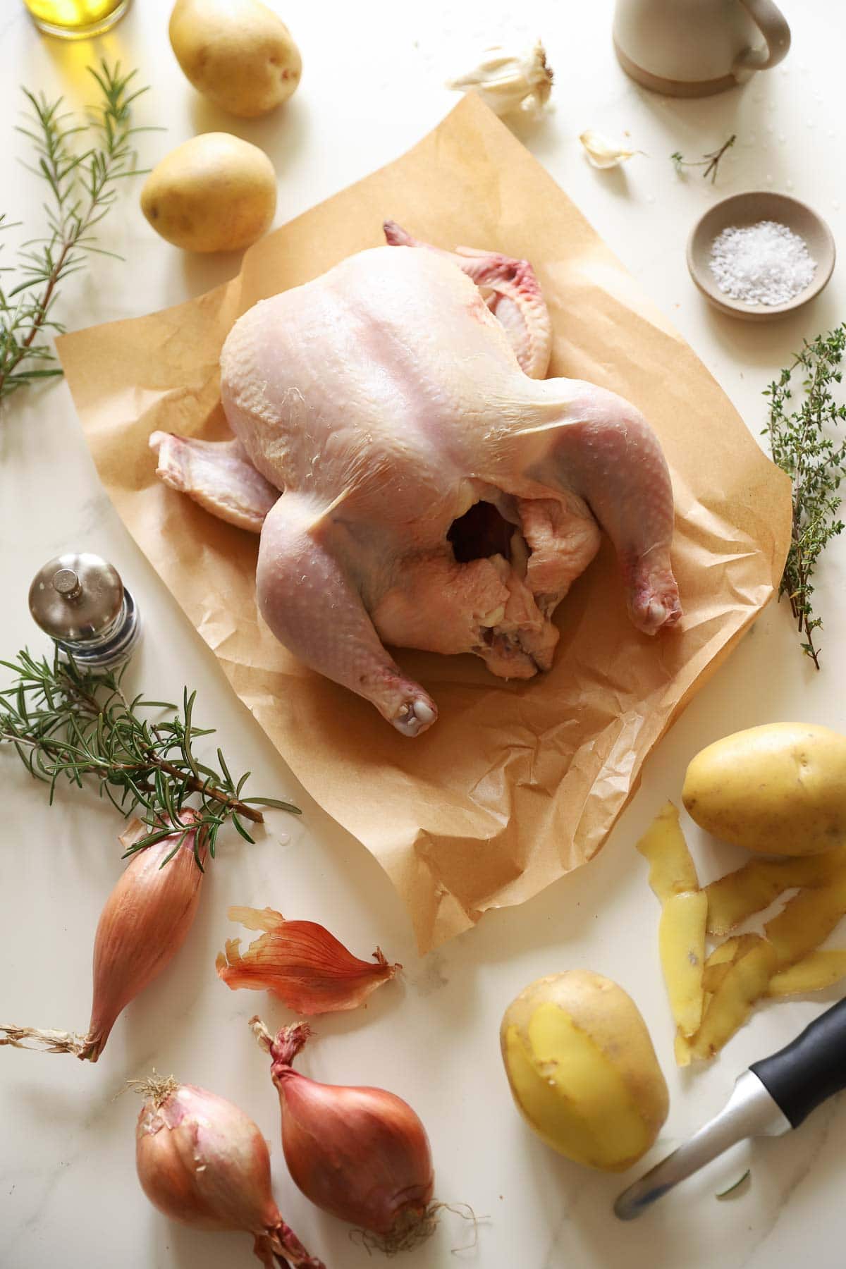 a raw whole chicken, thyme, salt and potatoes along with other ingredients on a counter