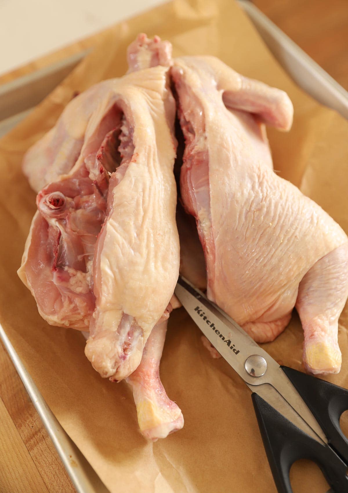 Kitchen shears cutting the backbone out of a whole chicken.