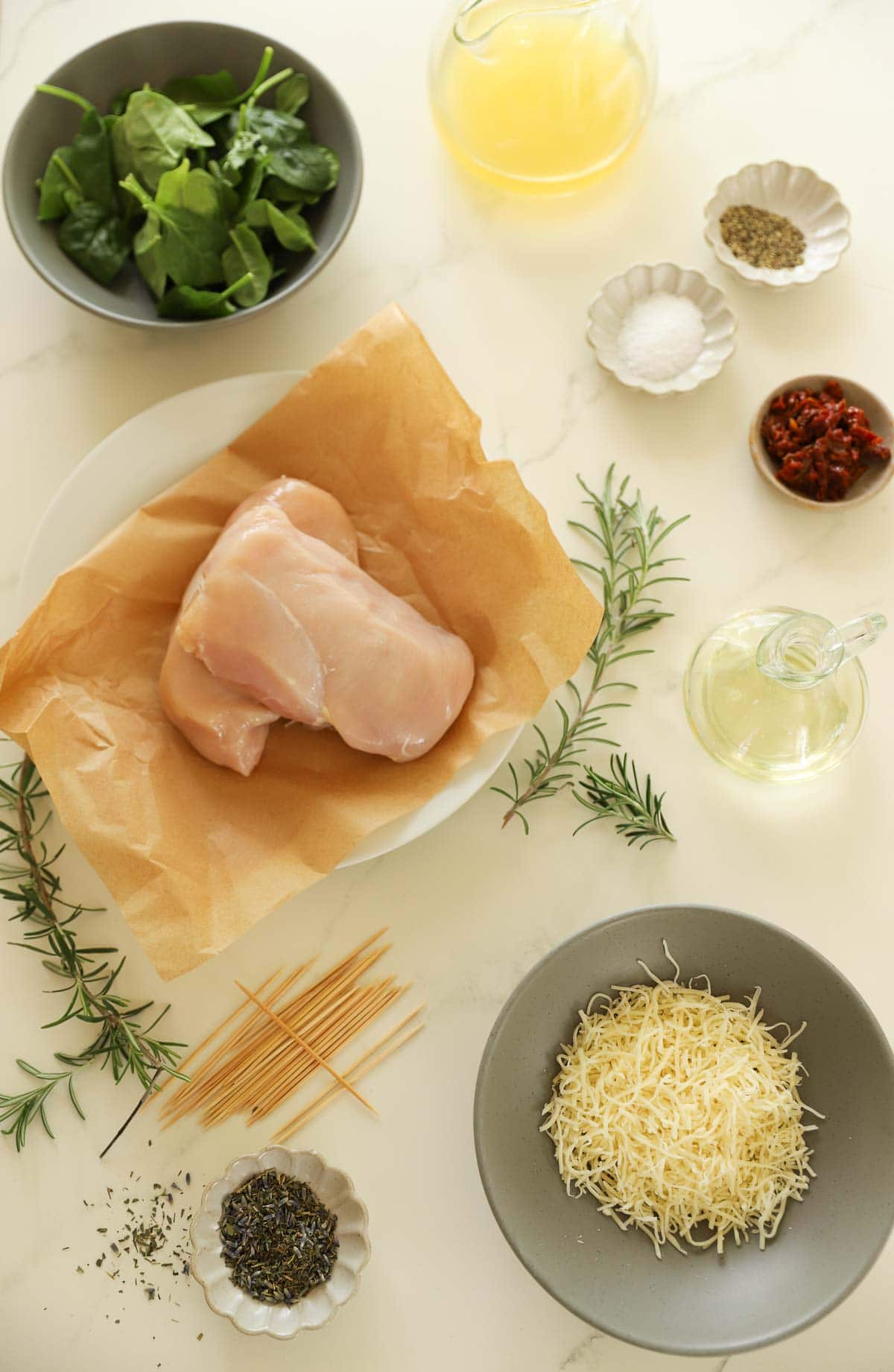 Chicken Breast, Spinach, Cheese, sundried tomatoes and herbs laid out on a counter top with other ingredients.