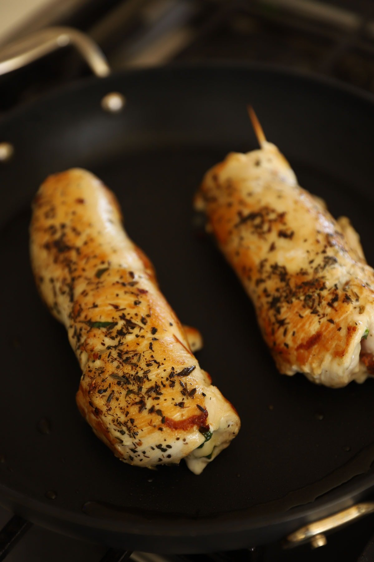 Stuffed chicken breasts searing in a non-stick pan.