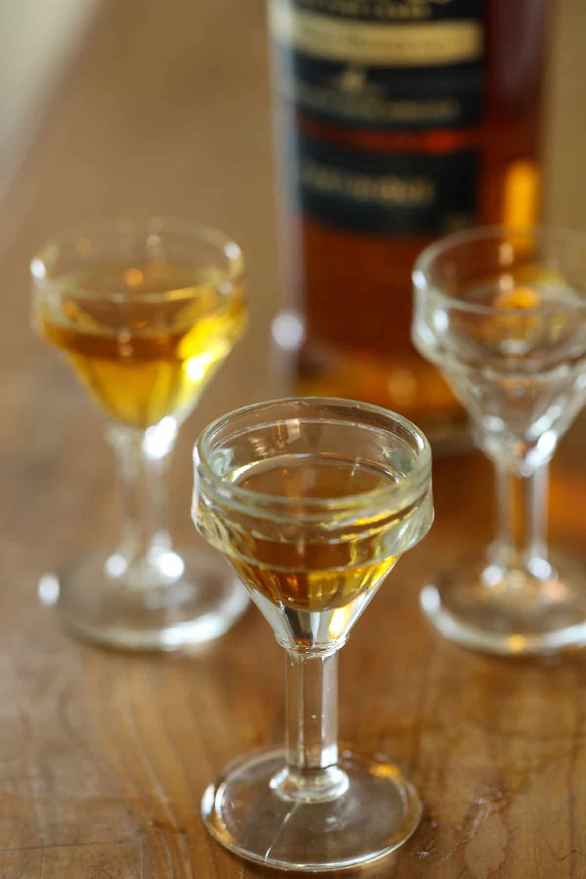 A bottle of dark rum on a table with shot glasses filled with rum.