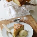 A whole cake on a cake stand with a slice of came on a plate with vanilla ice cream and a fork