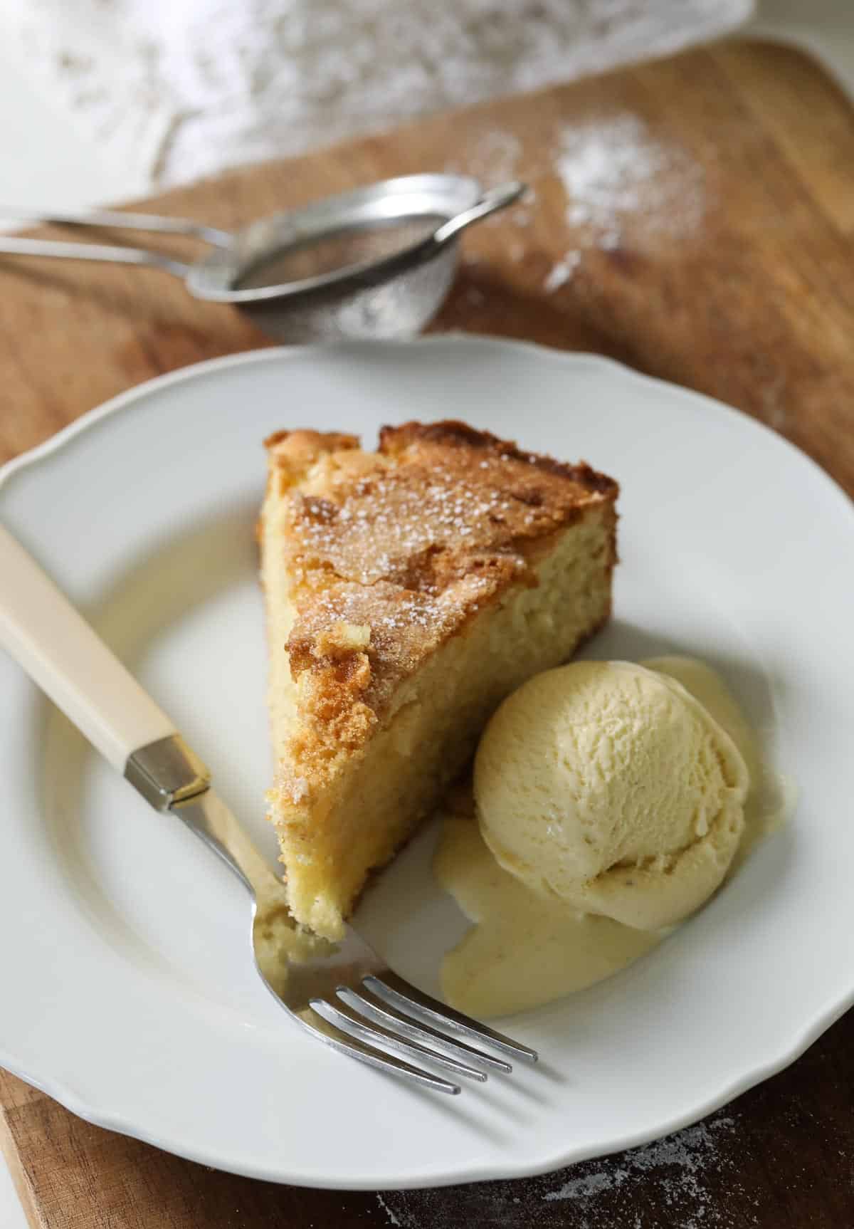 A slice of French apple cake on a plate with vanilla ice cream and a fork