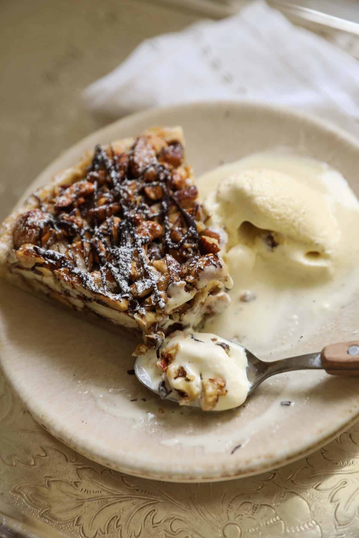 A slice of nut pie with a chocolate drizzle and vanilla ice cream