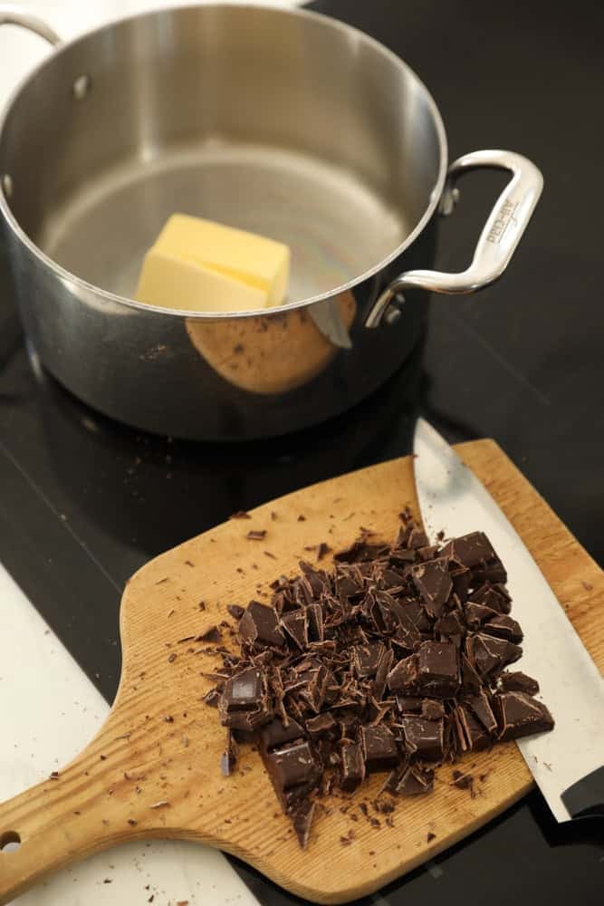 A Pot of butter on a cooktop with chopped chocolate on a cutting board