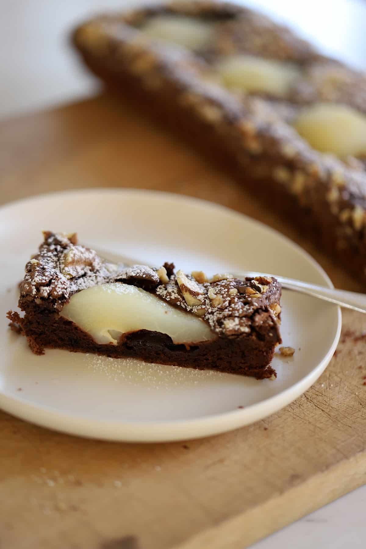 A slice of chocolate pear tart on a plate with a full tart behind it. 