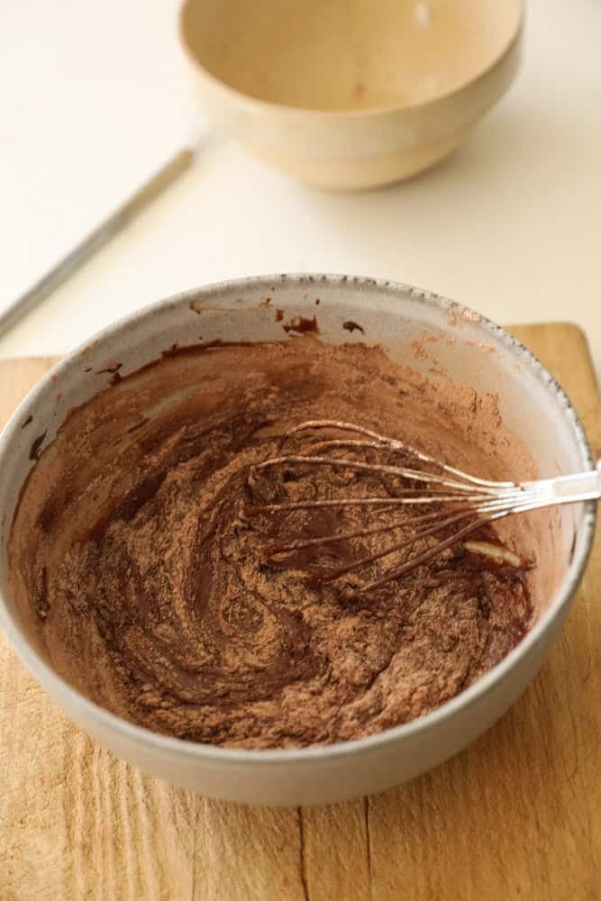 A bowl of chocolate batter with dry ingredients being whisked in.