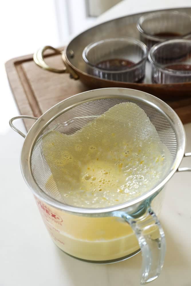 A fine mesh sieve catching solids while straining a custard base. 