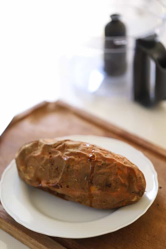 A baked sweet potato on a white plate and cutting board.