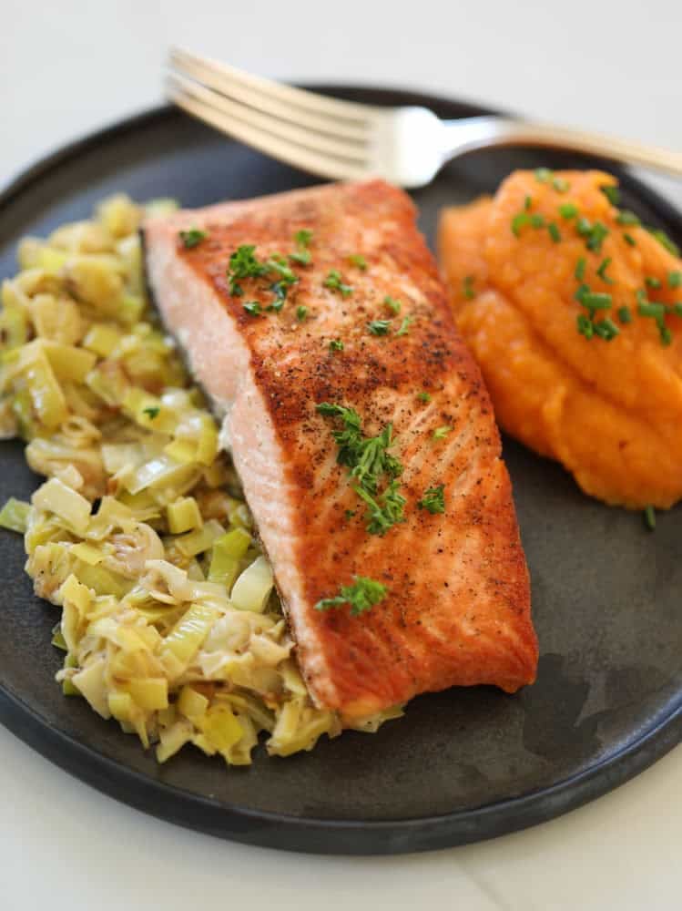 Pan seared salmon with leeks and sweet potato puree on a black plate.