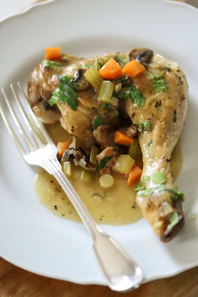 a chicken leg with white wine sauce and vegetables on a white plate