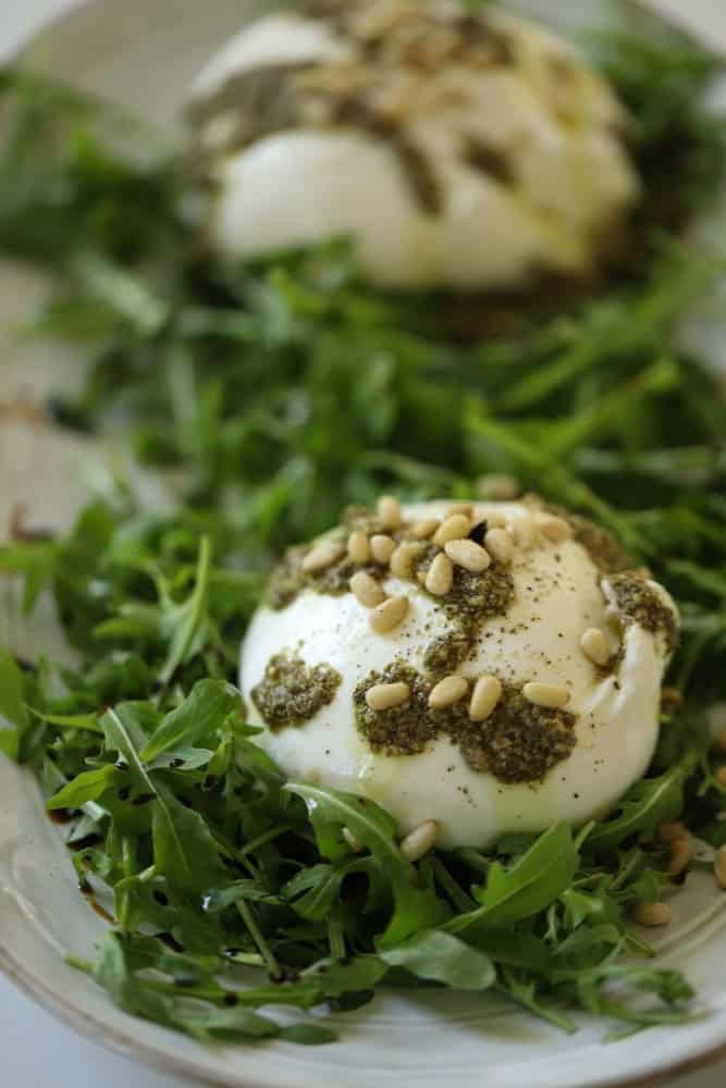 burrata drizzled with pesto topped with pine nuts on a bed of arugula.