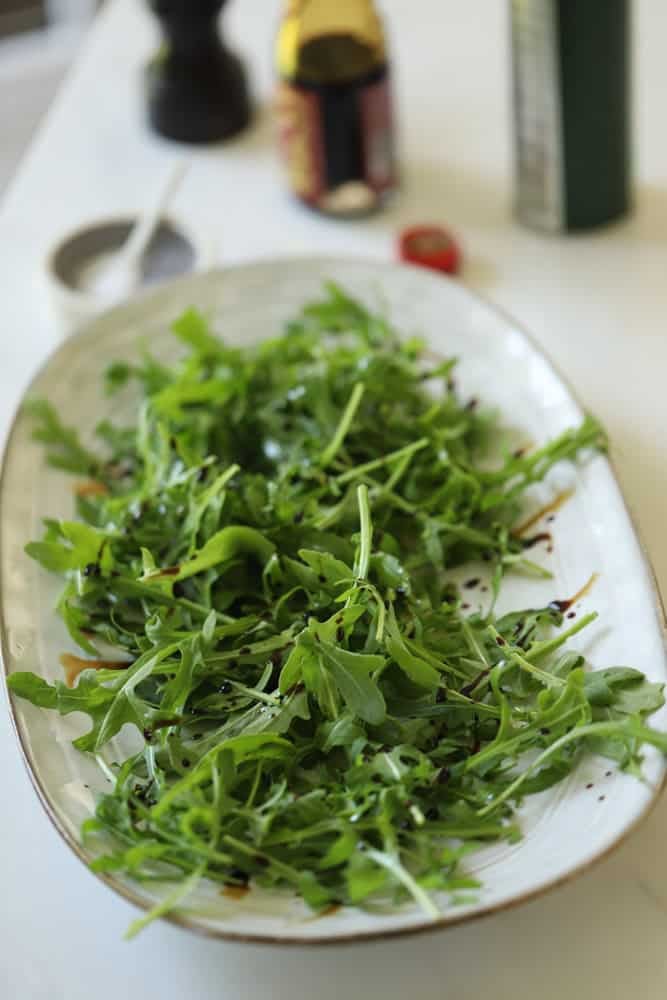 Rocket on a platter drizzled with balsamic vinegar and olive oil.