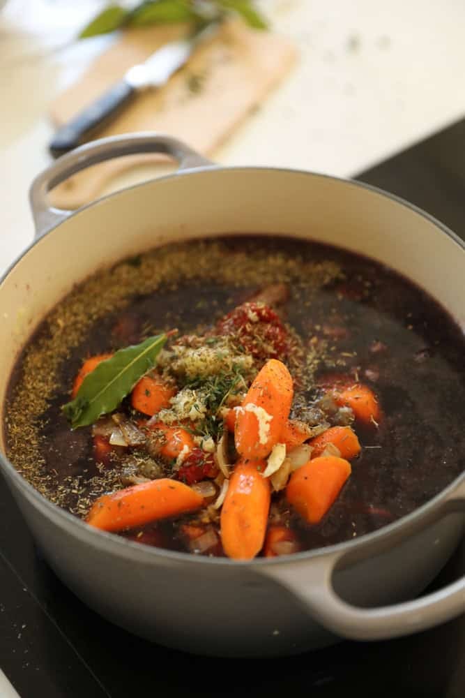 Wine, beef stock, stew meat, carrots, herbs and spices being added to a Dutch Oven.