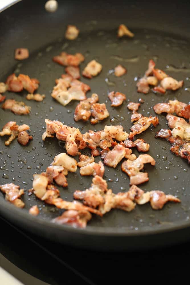 Bacon frying in a pan becoming crispy.