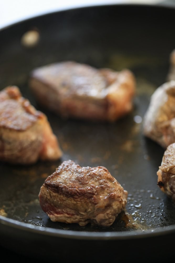 Searing pieces of beef in a non-stick pan.