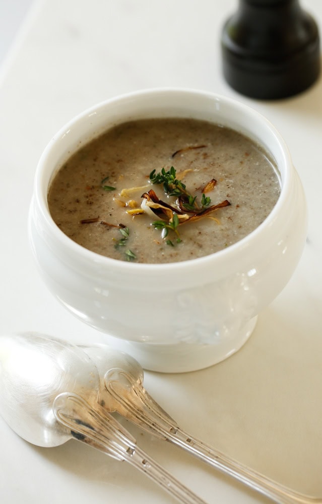 White Soup Bowl filled with Cream of Mushroom Soup with silver spoons and a pepper grinder in the background.