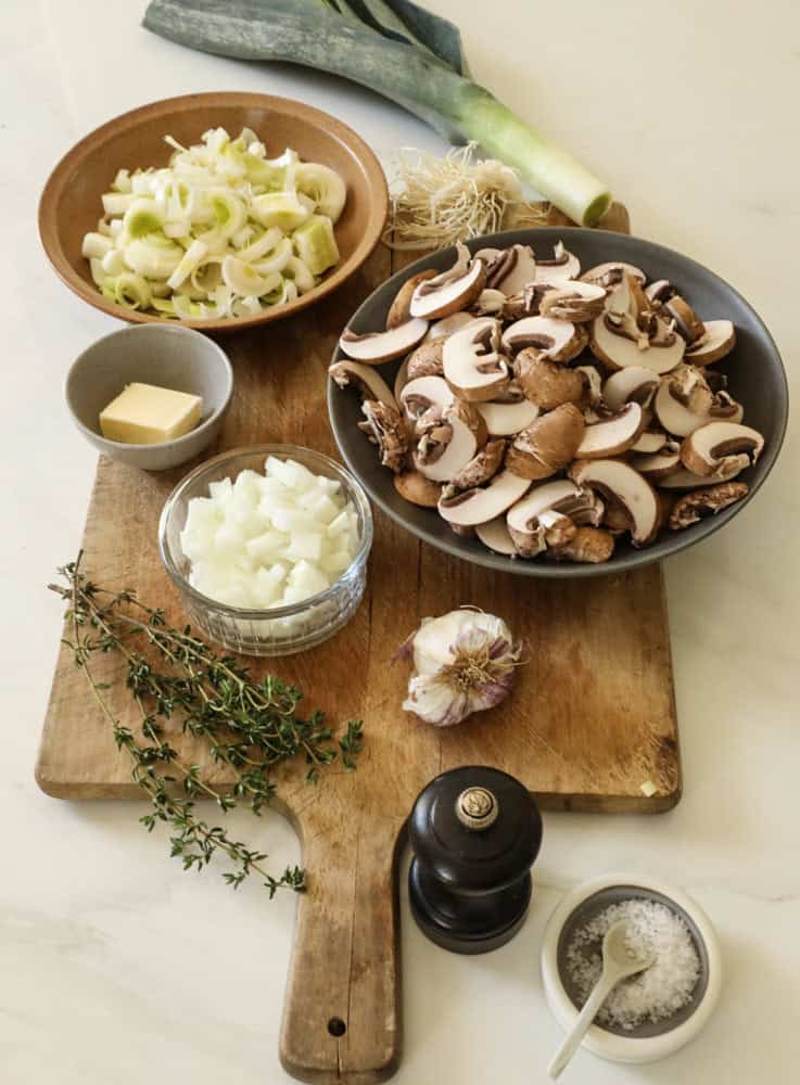 Mushrooms, leeks, garlic, onions, thyme, butter and seasonings laid out on a counter.
