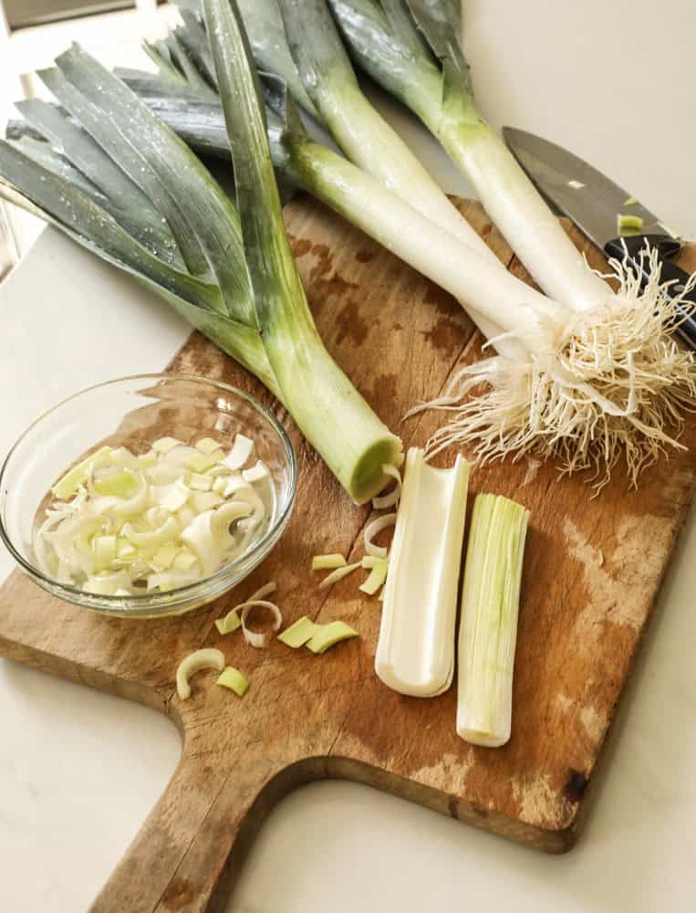 Sliced leeks on a cutting board and in a bowl of cold water.